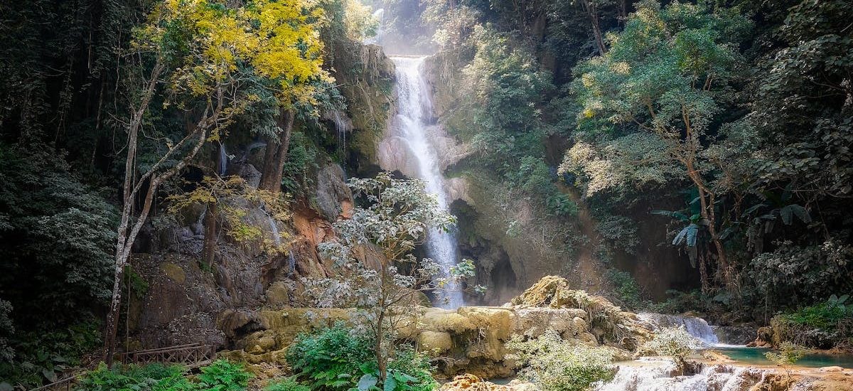 Serene waterfall cascading through dense jungle in Laos, surrounded by vibrant foliage.