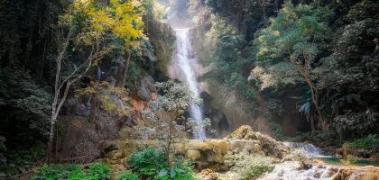 Serene waterfall cascading through dense jungle in Laos, surrounded by vibrant foliage.