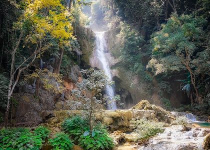 Serene waterfall cascading through dense jungle in Laos, surrounded by vibrant foliage.